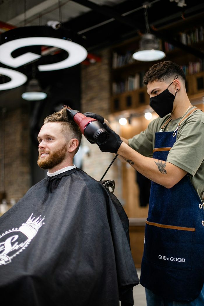 Barbier föhnt das Haar eines sitzenden Kunden