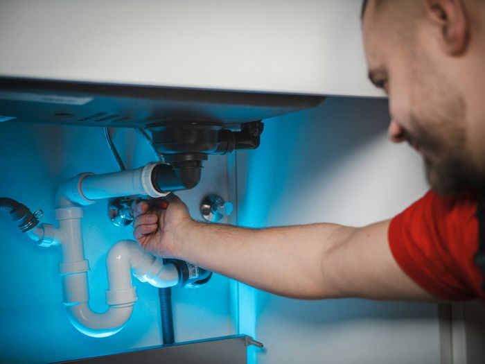 Klempner arbeitet an den Rohren unter einem Waschbecken